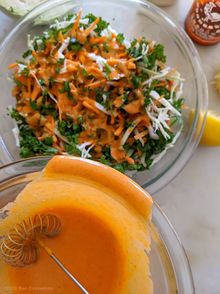 Pouring Sriracha dressing into kale slaw