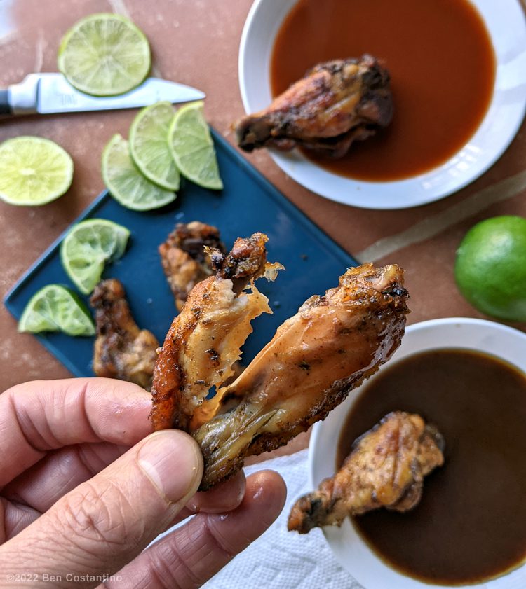 spicy lime chicken wings dipped in hot sauce with fresh lime wedges