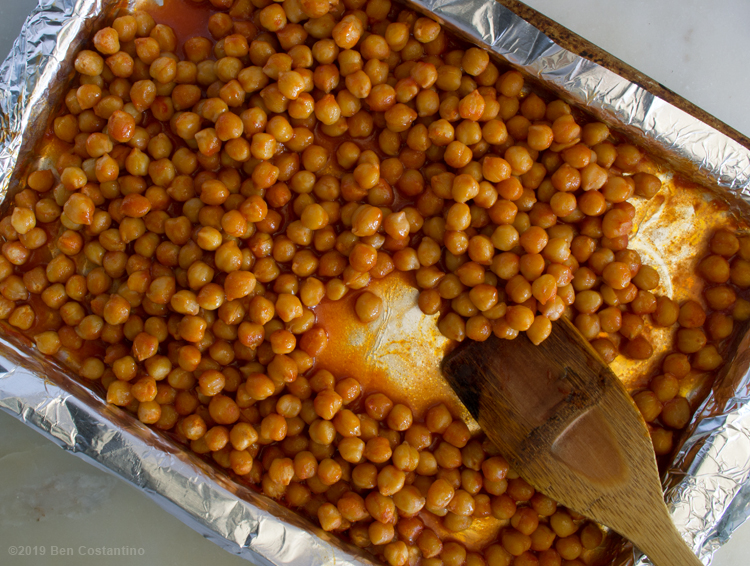 chickpeas being spread on a foil-lined sheet pan before roasting