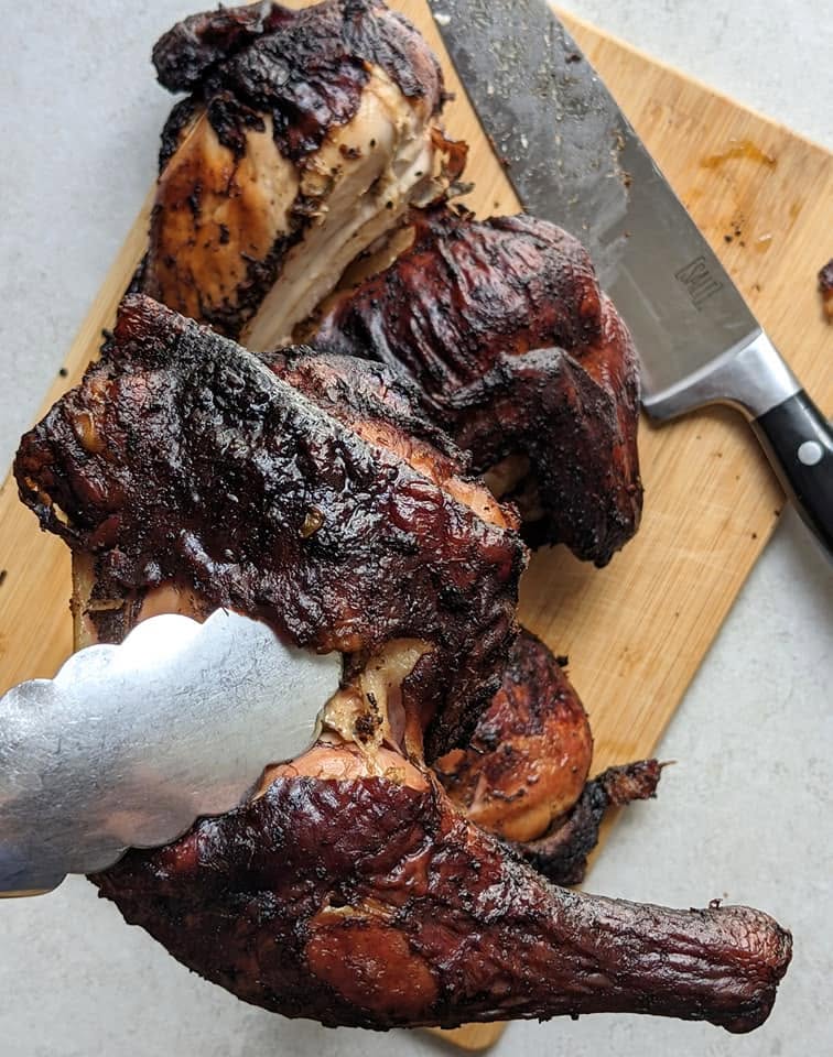 jerk chicken cooked to completion and tongs holding up a leg quarter