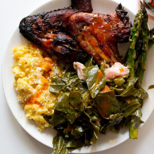 a plate of jerk chicken, Macaroni and cheese, collard greens and asparagus