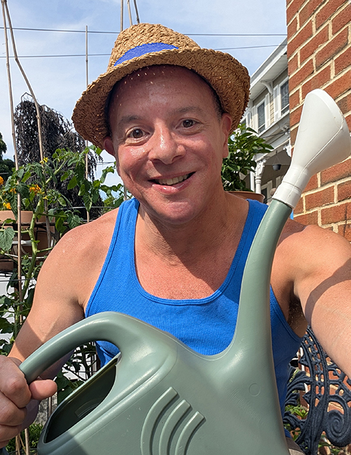 Photo of Ben holding a watering can in from ot homegrown tomato plants